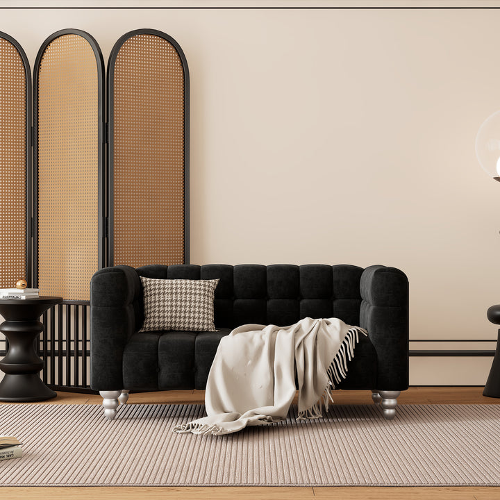 Black velvet sofa with tufted back and arms, silver feet, and a throw blanket and pillow.